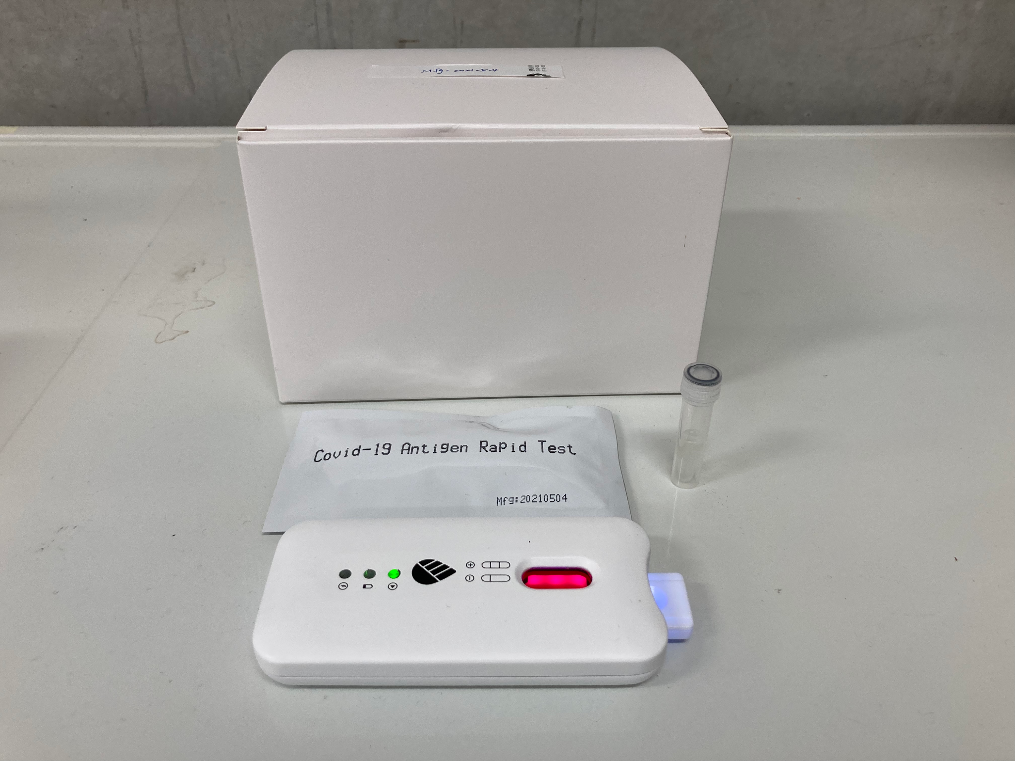 COVID-19 antigen rapid test pouch next to a compact lateral flow reader on a lab bench
