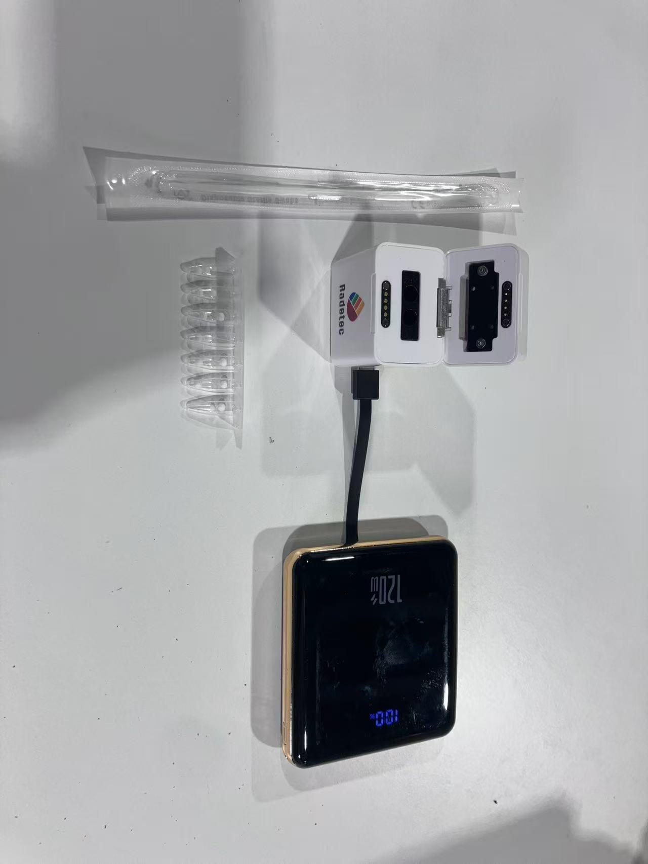 Open compact Radetec molecular reader beside sampling supplies and a battery pack